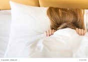 Frau im Bett zieht Decke über den Kopf
